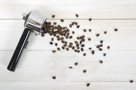 Portafilter handle with scattered coffee beans on wooden surface in top view.の写真素材