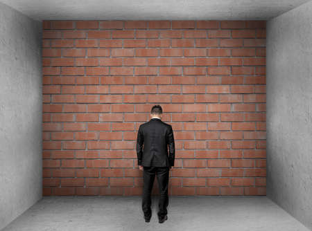 A businessman with bowed head stands in front of a brick wall in interior.の写真素材