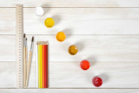 Top view of paint brushes with colorful gouache containers and pencils with centimeter ruler on a light wooden background.の写真素材