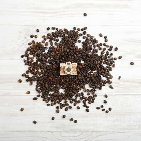 Small golden camera layout on a bunch of coffee beans in top view on wooden plankの写真素材