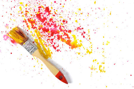 A paint brush with red and yellow gouache sprays near on white canvas in top view.