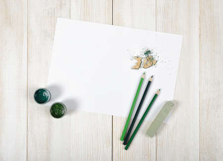 Top view of designer workplace equipped with green gouache jars, colored pencils, chalk, shavings and white paper on light wooden surface.の写真素材