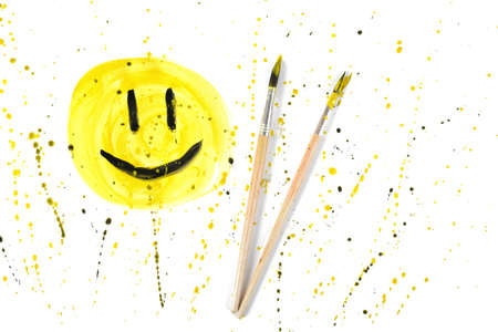Closeup smiley symbol with two used paint brushes on yellow spray background. Creative design.の写真素材
