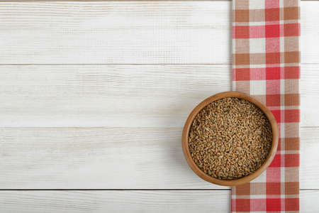 Pearl barley in a pot with red checkered  kitchen tablecloths on the right side on wooden surface. Top view.の写真素材