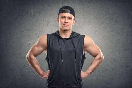 Waist-up portrait of smiling handsome muscled young man with his hands on hips looking directly at the cameraの写真素材
