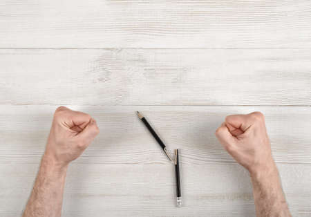 Closeup masculine fists clenched on wooden panel in top view. Anger sign.の写真素材