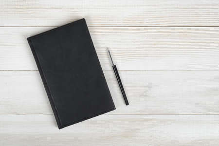 Flat lay of black notebook and black pen on light wooden surface. Composition.の写真素材