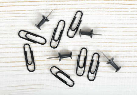 Closeup black thumbtacks and clips on light wooden surface. Stationery.の写真素材
