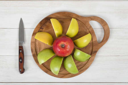 Ripe juicy color apples lie on a wooden board with a knife next to it in top viewの写真素材
