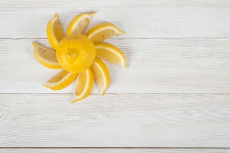 Top view of yellow citrus slices laid out into the sun shape around the whole lemon on  light wooden surface.の写真素材