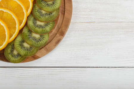 Orange and kiwi are cut into slices and well decorated on a cutting board. Top view with copy space.の写真素材