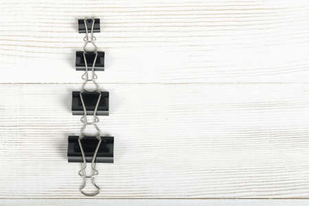 Black binder clips posted from the biggest to the smallest on a wooden surface with copy space on the right side in top view.の写真素材