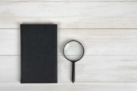 Flat lay of black notebook and magnifying glass on light wooden surface. Composition. Office...