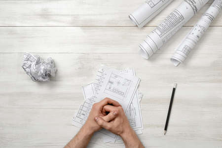 Closeup masculine folded hands on wooden panel with hand-folding a piece of paper. Worry process. Top view composition. Anger sign. Workplace of architect or constructor. Engineering work. Construction and architecture. Architect drawing. Draft.の写真素材