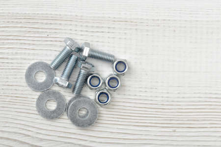 Layout with nuts, bolts and washers distributed on wooden surface with copy space. Top view of construction tools. Mend and repair. Parts for repair. Fixing stuff.の写真素材