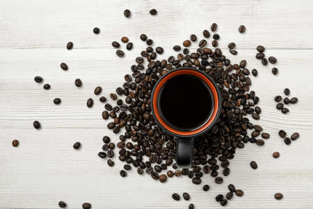 Cup of hot coffee on a wooden surface with spreaded coffee beans. Top view. Workplace. Willingness to work overtime. Increasing productivity in the mornings. Improving mood and productivity. Art composition. Concept.の写真素材