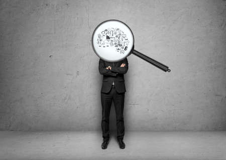 Businessman stands with folded arms with magnifier instead of head. Economic and statistical graphs displayed through the magnifier. Deep research. Full concentration. Business idea. The beginning of the business plan. The obsession with the business ideaの写真素材