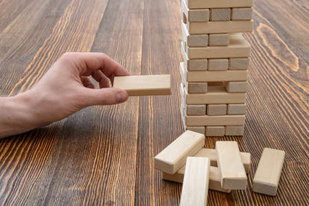 Close-up hands of man playing with wooden bricks. Entertainment activity. Education and development. Full concentration. Game of physical and mental skill. Removing blocks from a tower. Keeping balance.の写真素材