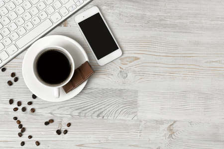 Keyboard, cup of hot coffee and smartphone on wooden surface with copy space. Workplace of office man. Office stuff. Willingness to work overtime. Conductive working environmentの写真素材