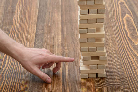 Close-up hands of man pulls out wooden bricks. Removing blocks from a tower. Keeping balance. Full concentration. Entertainment activity. Game of physical and mental skill. Close-up photo.の写真素材