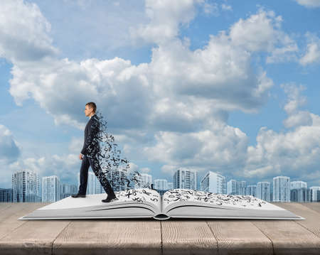 Side view of young businessman walking on an open book with a plume of letters. Gaining knowledge. Useful information. Business reading. Office clothes. Education concept.の写真素材