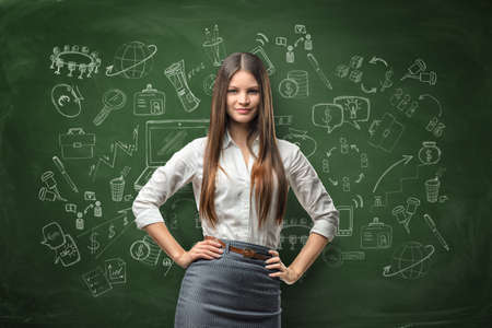 Young businesswoman looks directly at the camera and smiles on the background of the blackboard with chalk drawings. Cutout portrait. Successful lifestyle. Business training. Education and learning.の写真素材