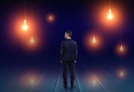 Back view of a businessman looking upwards at light bulbs glowing in the dark.の写真素材
