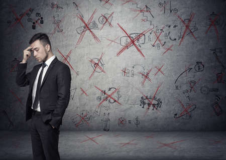 Businessman stands pondering on the concrete background with depicted ideas that crossed with red.の写真素材