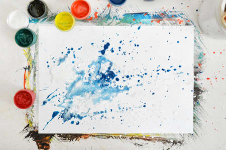 Top view of an artist's workplace with a sheet of paper with splashes of blue and white and jars of different paint.の写真素材