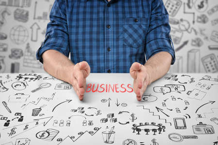 Close-up hands of a sitting man with word 'business' between them and business doodles on the table and on the background.の写真素材