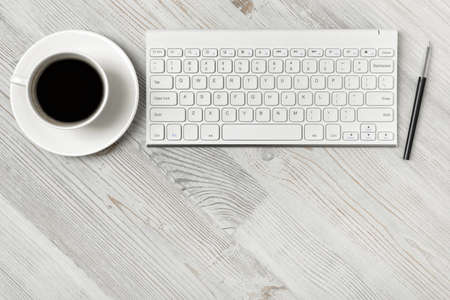 Top view of a workplace with a keyboard, a cup of coffee and a pen on a wooden table.の写真素材