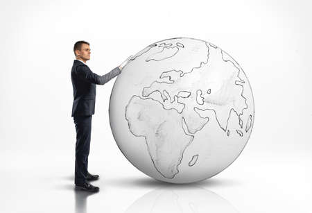 Businessman standing next to a large world globe with an outline of Africa and Europe over a white backgroundの写真素材