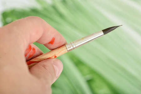 Close-up hand of man holding paint brush on green gouache background.
