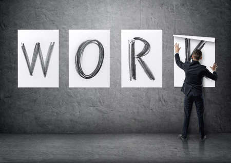 Businessman putting up posters with letters on a concrete wall that form a 'work' word.の写真素材