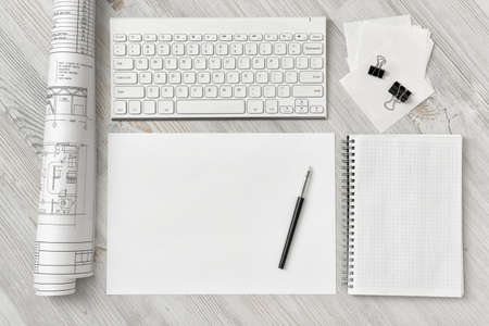 Top view of a draftsman's workplace with a keyboard, a sheet of paper with a pen, a notebook and...