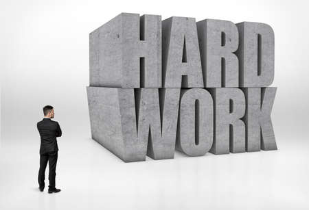 Back view of a businessman looking at big concrete 3D words 'hard work' isolated on white background.の写真素材