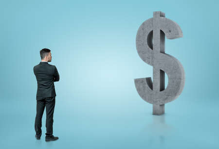 Back view of a businessman looking at big concrete dollar.の写真素材