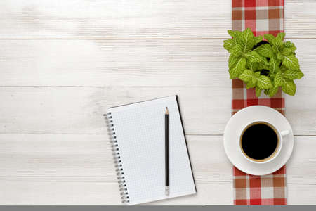 Office workplace with green houseplant on checkered tablecloth, cup of coffee and empty notebook. Top view composition.の写真素材