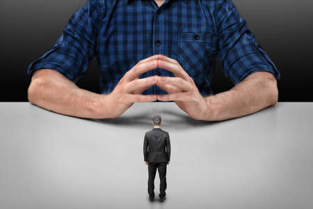 Businessman stands in front of a cropped portrait of a big man sitting with his fingers clasped.の写真素材