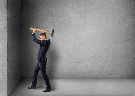 Side view of a businessman crashing concrete wall with hammer.の写真素材