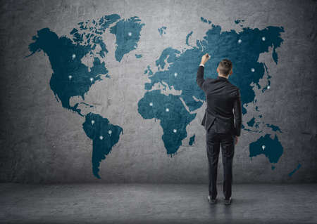 Back view of a businessman making marks on world map.の写真素材
