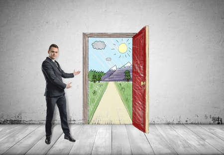 Businessman stands showing sunny scene with the road and mountains behind an open door by both hands.の写真素材