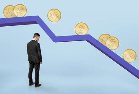 Businessman with his head bowed standing under falling graph with golden coins rolling down.の写真素材