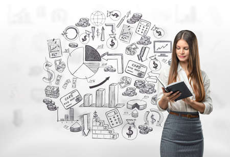 Cropped portrait of young businesswoman looking in her note book on the background of business doodles.の写真素材