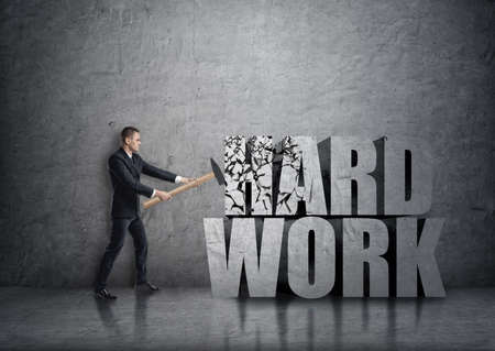 Side view of young businessman crashing 3D concrete 'hard work' words with a hammer.