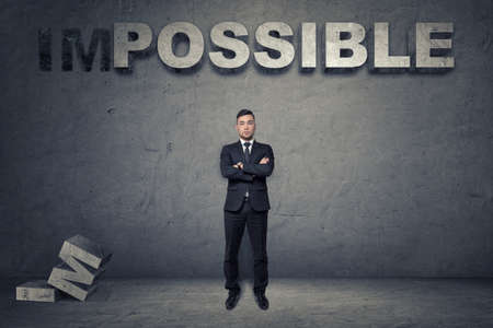 Front view of a businessman standing with folded arms under big 3d concrete word 'possible'.の写真素材