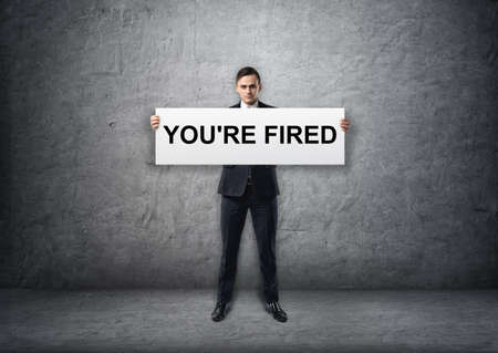 Businessman holding banner with 'you're fired' text on it in his hands.の写真素材