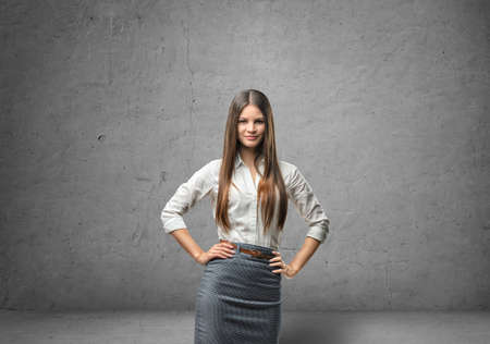 Cropped portrait of a young businesswoman holding her hands on her waist in the background of a concrete wall.の写真素材