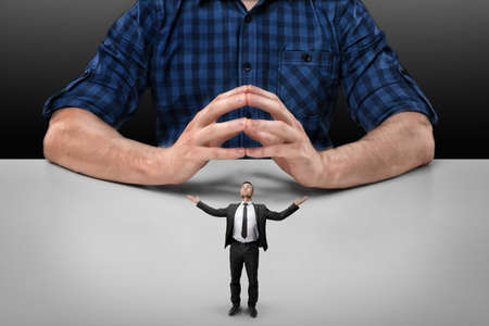 Businessman stands with raised hands in front of cropped portrait big man sitting with his clasped fingers.の写真素材