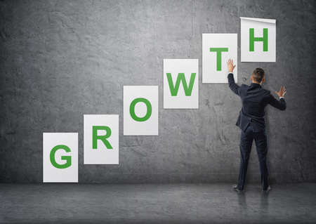 Businessman putting up posters with letters on a concrete wall that form a 'growth' word.